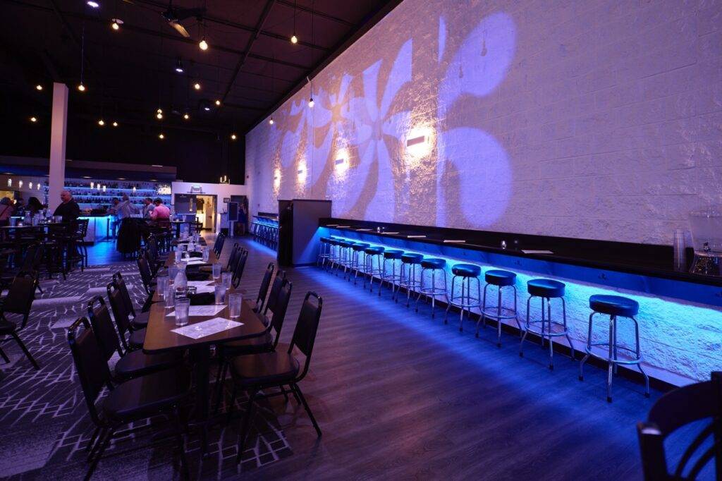 Venue seating beside a blue-lit bar and projection wall