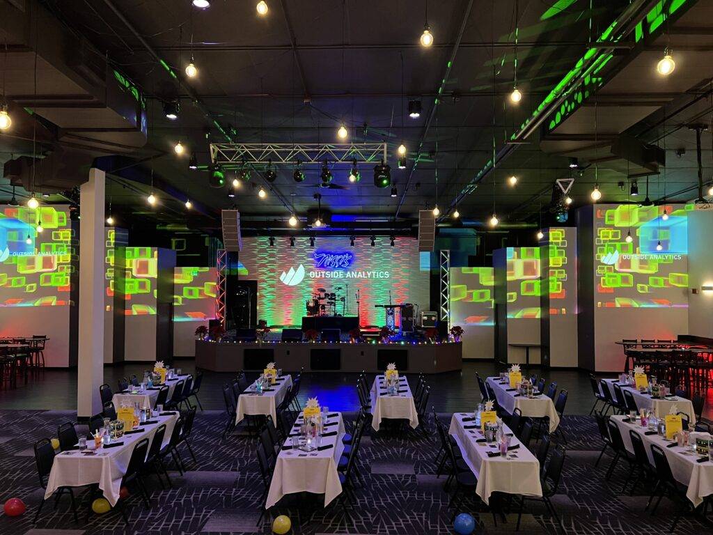 Dining tables facing a stage and colorful company projections at Nissi’s