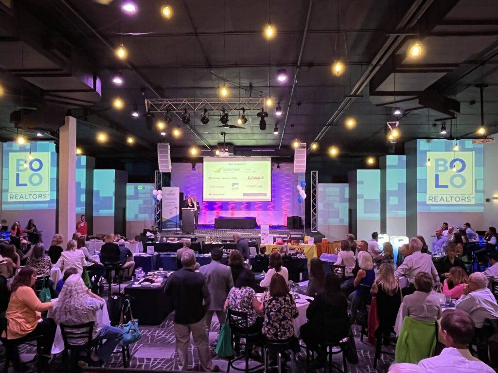 Guests seated at tables facing a speaker on Nissi’s stage