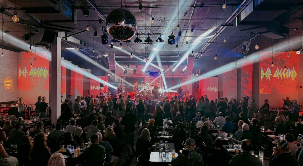Seated audience beneath white stage lights and a mirrored ball