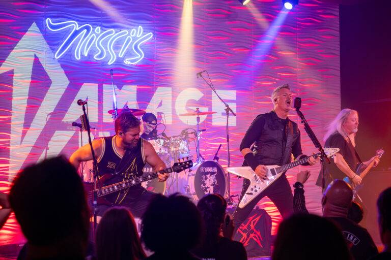 Musicians performing in front of the illuminated Nissi’s stage sign