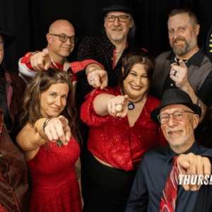 Group of smiling band members in red/black outfits pointing at the camera, promotional photo for Midnight Hour Band NOCO poster.
