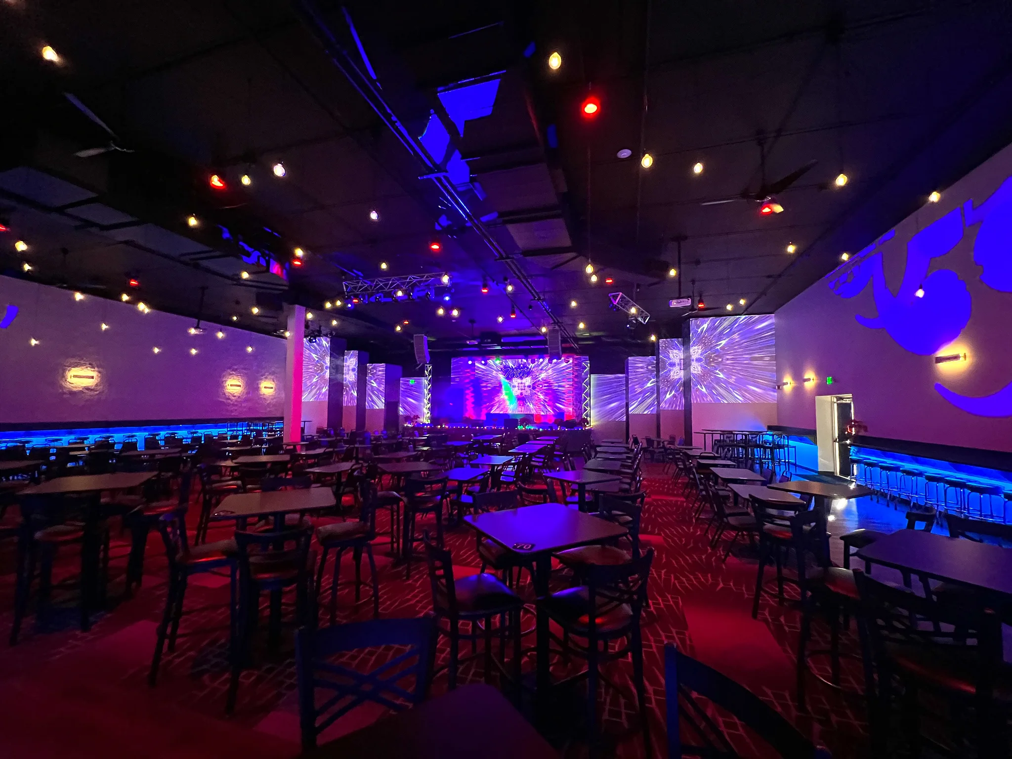 Tables and chairs facing Nissi’s stage beneath blue and purple lighting