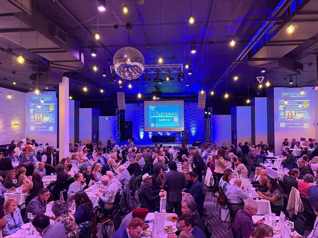 Fundraiser guests seated at tables facing Nissi’s stage and projection screens
