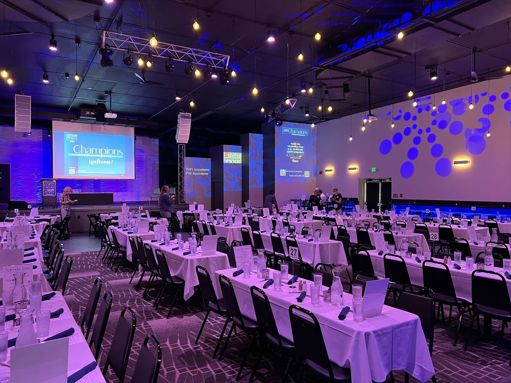 Fundraiser tables arranged beneath projection screens in Nissi’s event room
