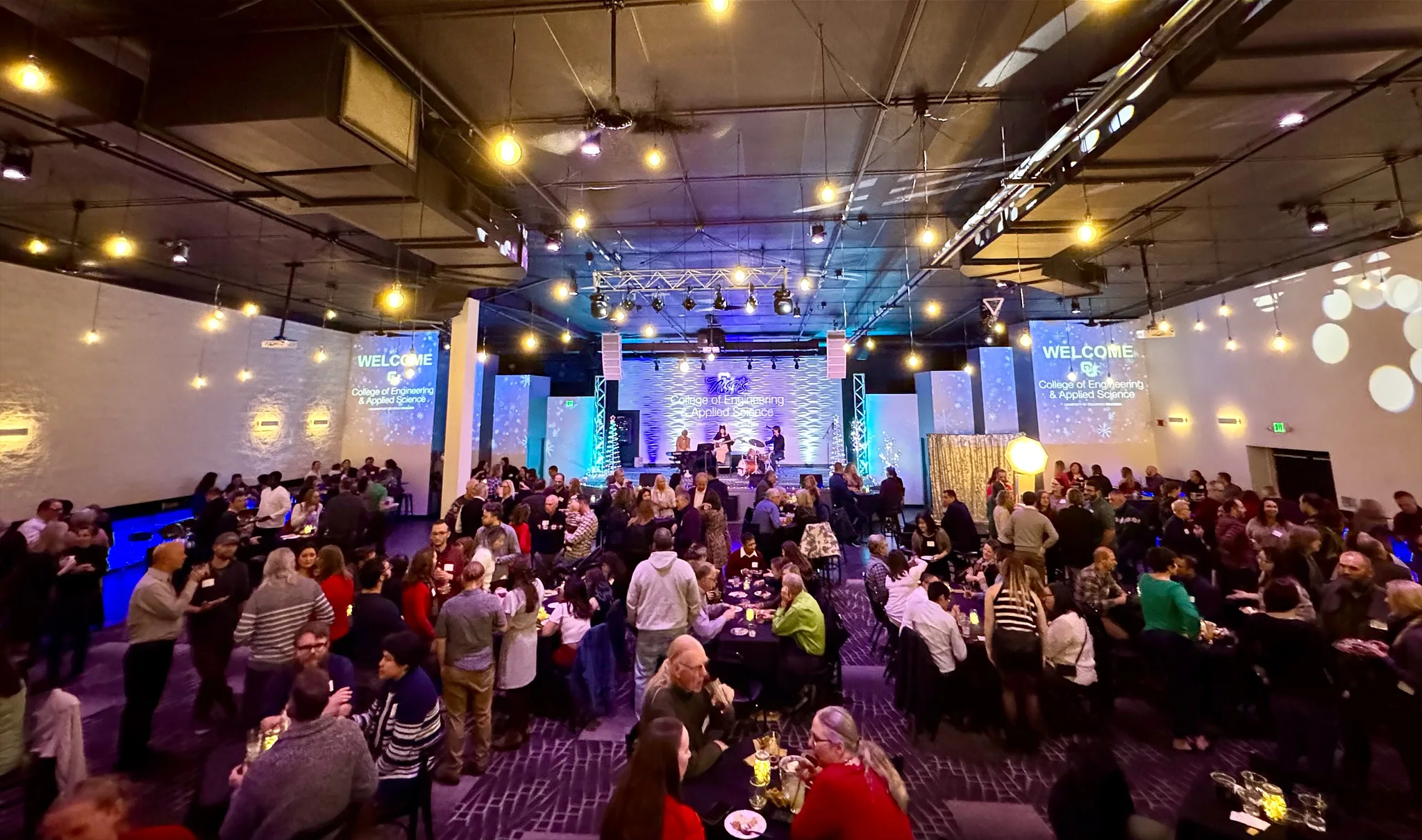 Holiday party guests gathered around tables beneath warm lights at Nissi’s
