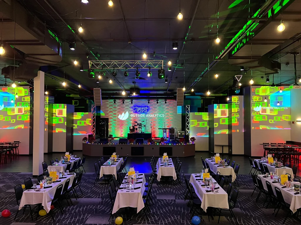 Tables facing the stage and projections for a company holiday party at Nissi’s