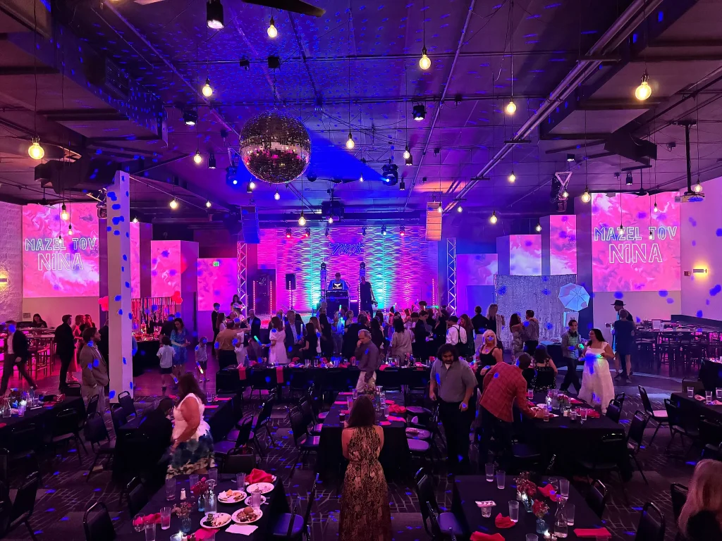 Mitzvah guests seated beneath colorful projections in Nissi’s event room