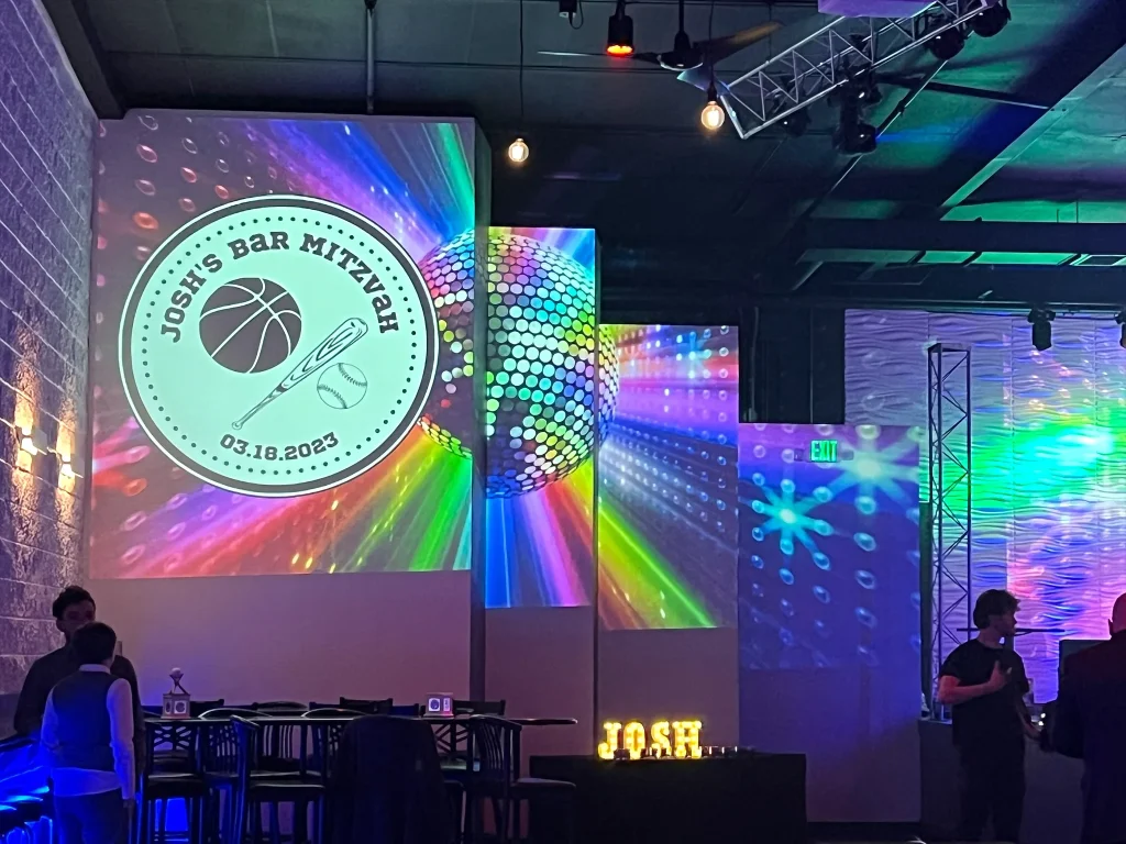 Personalized mitzvah projection screens beside Nissi’s stage